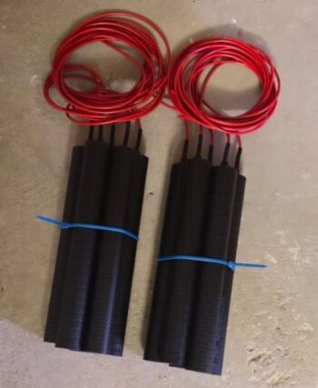 Two black, cylindrical electronic modules with red insulated wires coiled on top, placed on a concrete floor and secured with blue zip ties.